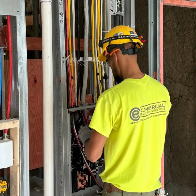 CES electrician in a yellow hard hat wiring a framed wall